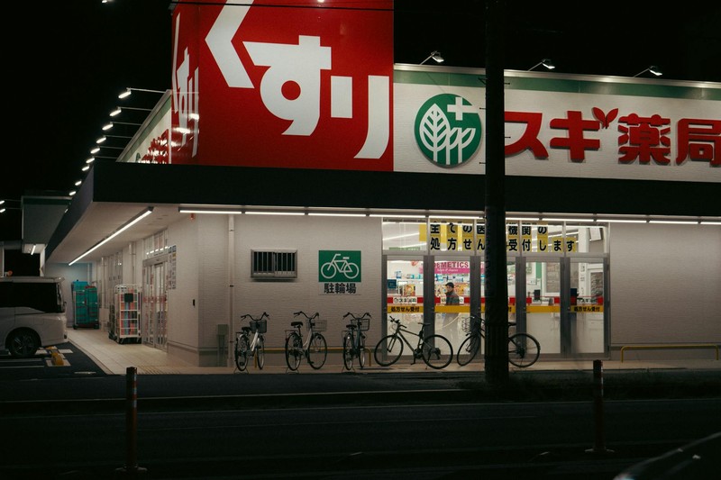 A Sugi Pharmacy storefront at night in Toyohashi, Aichi, Japan, with bicycles parked outside