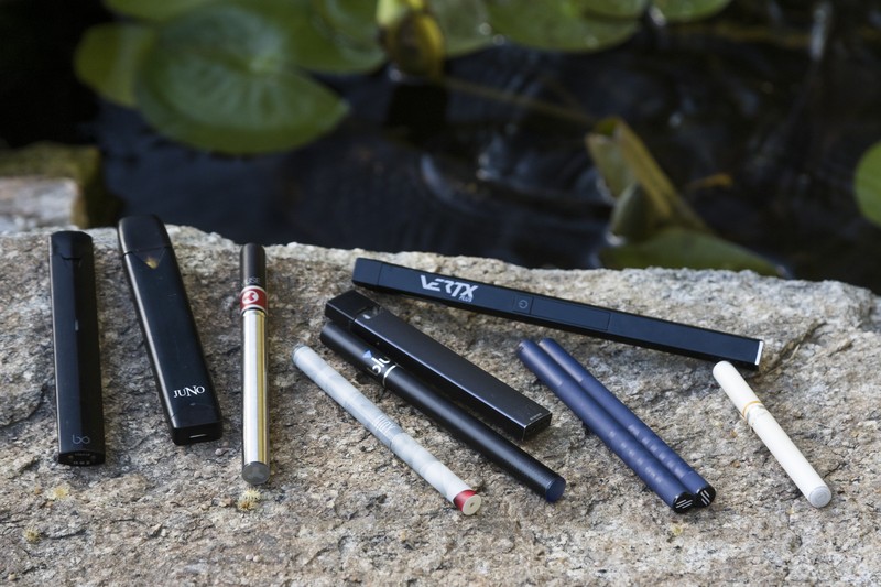An assortment of electronic cigarettes and vaping devices from various brands arranged on a stone surface