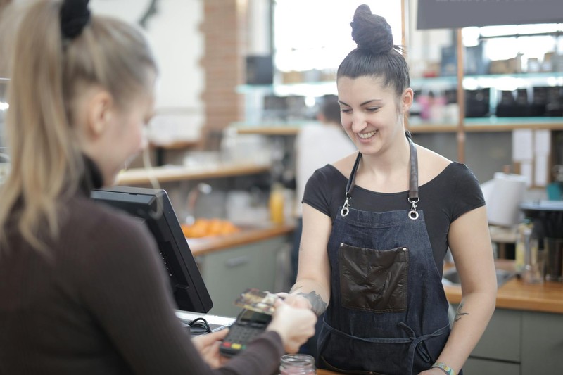 A smiling young retail worker hands a receipt to a customer at a cash register counter