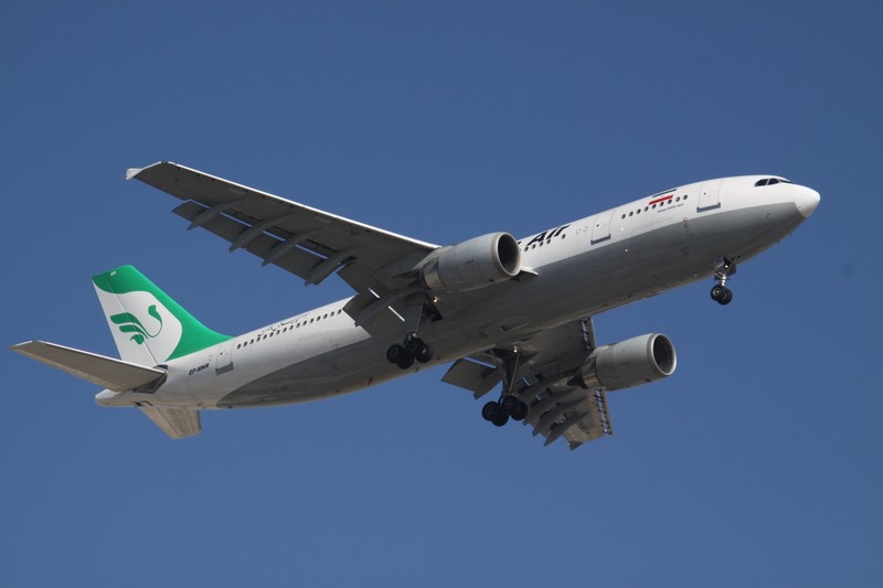 An Iran Air commercial jet in flight with landing gear deployed against a clear blue sky