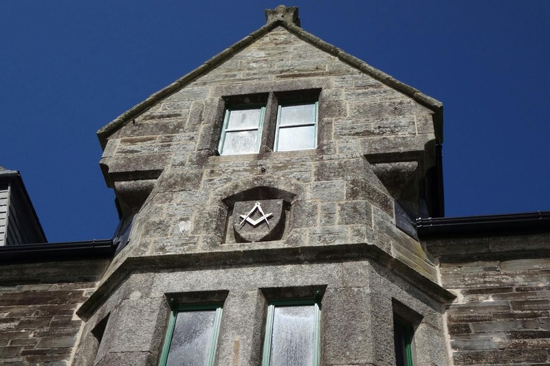 A historic stone Masonic lodge building with a square and compass emblem carved above the windows
