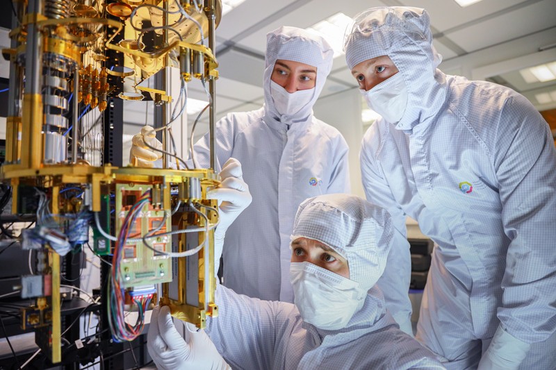 Technicians in cleanroom suits assemble the cryogenic cooling system of a quantum computer in a laboratory