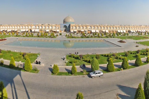 Aerial view of Naqsh-e Jahan Square in Isfahan, Iran, showing the central reflecting pool, gardens, and surrounding historic architecture under a hazy sky.