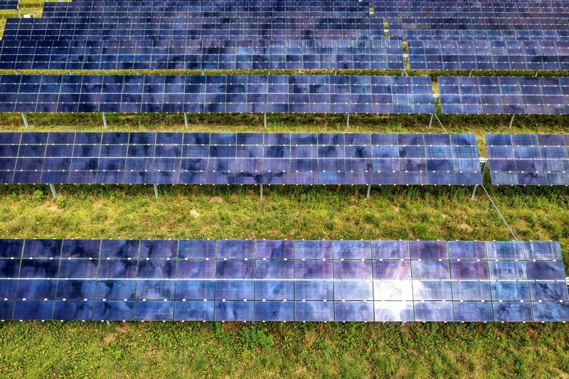 Aerial drone view of rows of solar panels stretching across a large solar farm surrounded by green grass