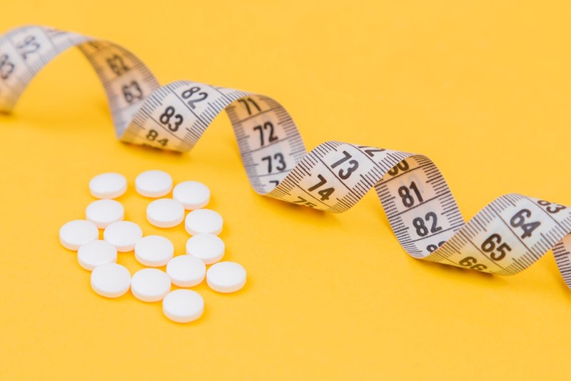 White pills arranged next to a coiled measuring tape on a bright yellow background