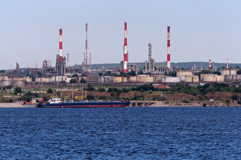 Saratov Oil Refinery along the Volga River with smokestacks, storage tanks, and a cargo vessel moored nearby