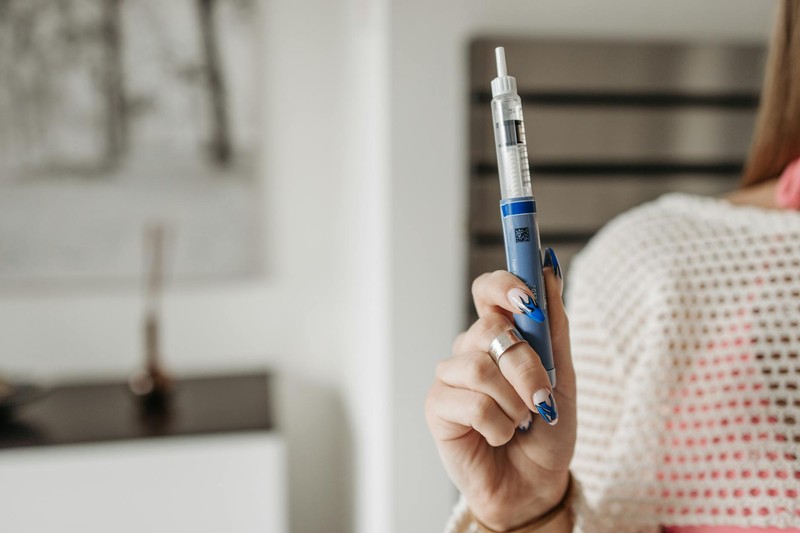 A person's hand holding a blue injection pen against a softly blurred indoor background