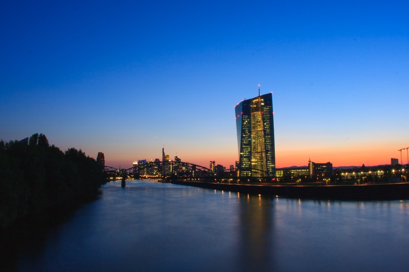 The European Central Bank headquarters in Frankfurt glowing at twilight with the city skyline reflected in the Main River