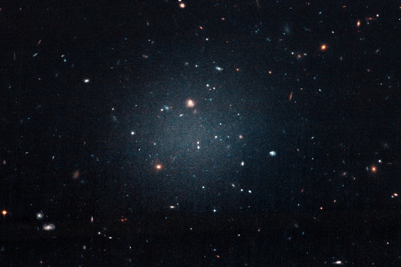 Hubble Space Telescope image of a ghostly, diffuse galaxy lacking dark matter, showing scattered faint stars against deep blue space