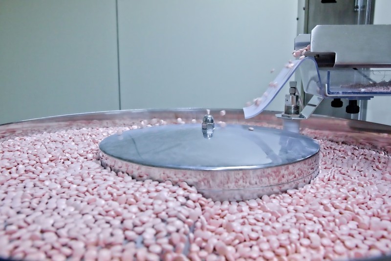 A stainless steel pharmaceutical coating pan filled with pink drug pellets during tablet manufacturing