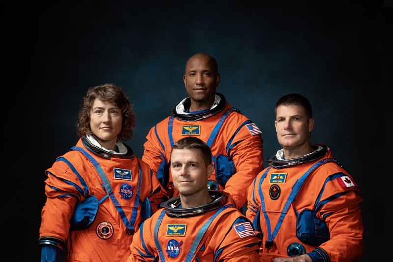 The four Artemis II astronauts posed in orange flight suits against a dark blue background