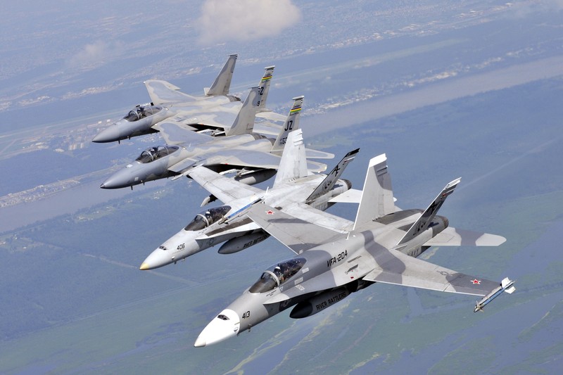 Four US military fighter jets flying in echelon formation over a coastal landscape