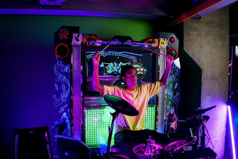 A person playing a drum-based rhythm arcade game under neon lights