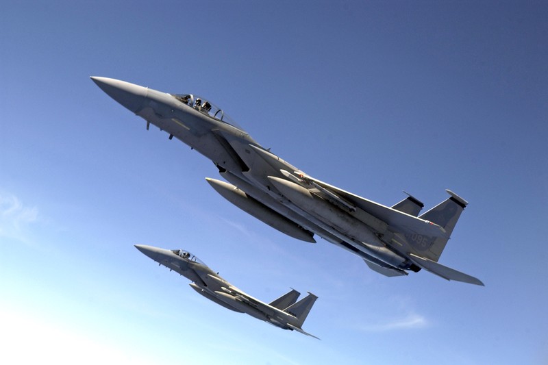 Two U.S. military fighter jets flying in escort formation against a clear blue sky