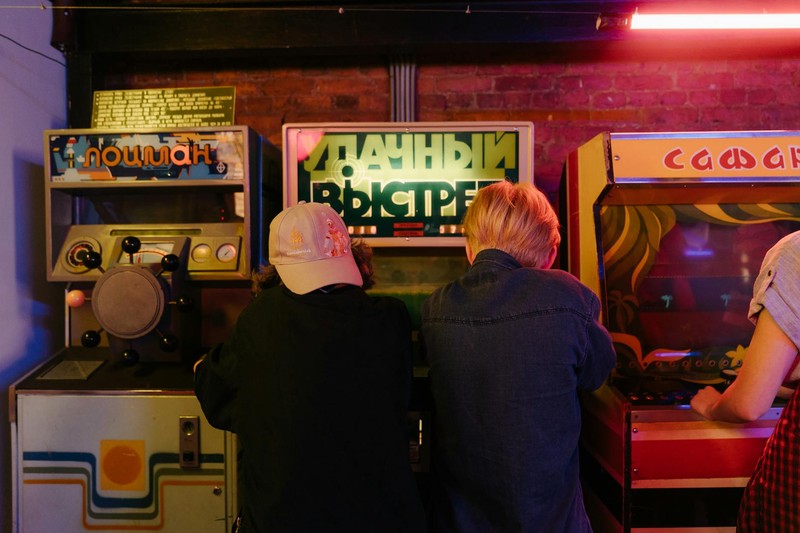 Teenagers playing vintage arcade machines in a dimly lit retro arcade