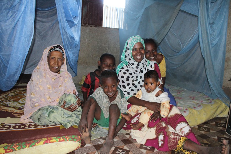 A family gathered under blue mosquito netting inside a modest home in Ethiopia