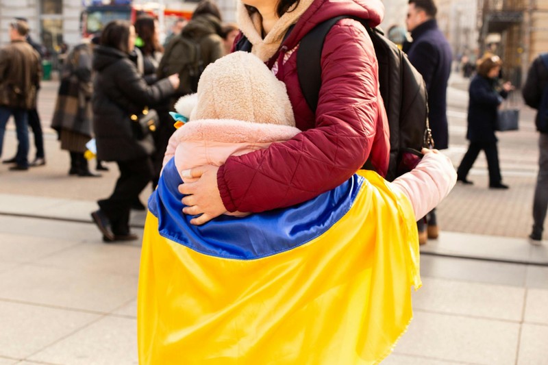 An adult protectively holds a child wrapped in a Ukrainian flag in a public square