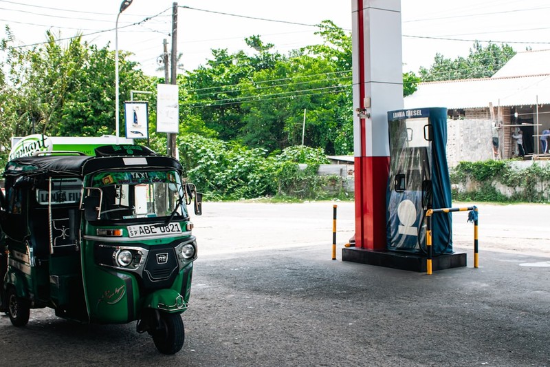 A fuel dispenser at a petrol pump in Sri Lanka with a green auto-rickshaw parked alongside