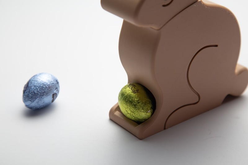 A brown bunny figurine holding a shiny green foil-wrapped Easter egg on a neutral background