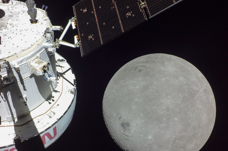 The Orion spacecraft with its solar panels extended, seen against the cratered surface of the Moon in the blackness of space during the Artemis I mission.