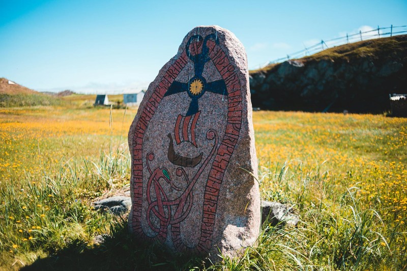 An ancient Viking runestone with carved ornaments standing in a blooming meadow under a blue sky