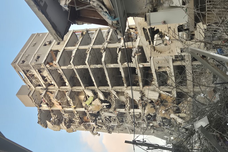 A partially collapsed multi-story building in Bat Yam, Israel, with exposed concrete framework and scattered debris after an Iranian missile strike