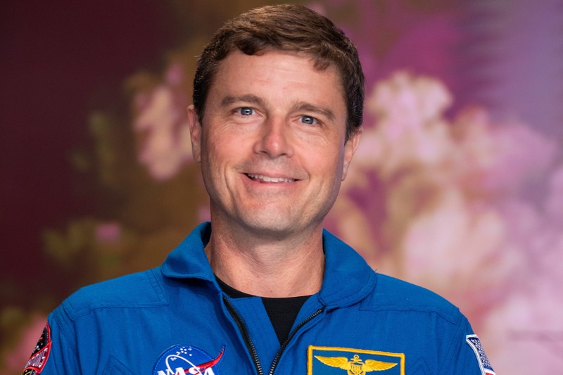 NASA astronaut and Artemis II commander Reid Wiseman smiling in a blue NASA jumpsuit at a Kennedy Space Center news conference
