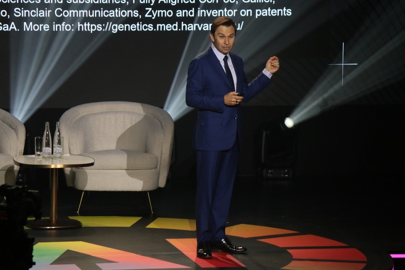 David Sinclair speaking on stage at a conference with Harvard Medical School referenced on the backdrop