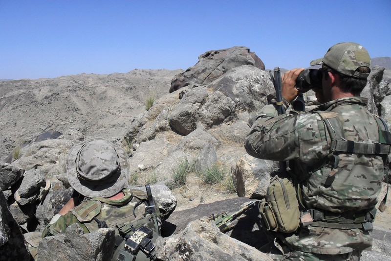 Two Australian special forces soldiers in tactical gear observing a rugged, arid valley in Afghanistan