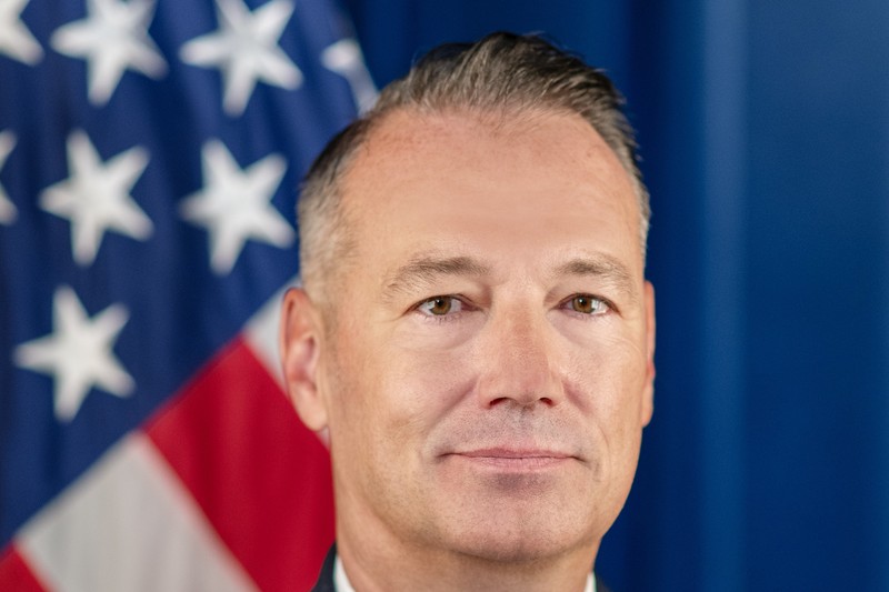 Formal portrait of Todd M. Lyons, Acting Director of U.S. Immigration and Customs Enforcement, standing before an American flag.