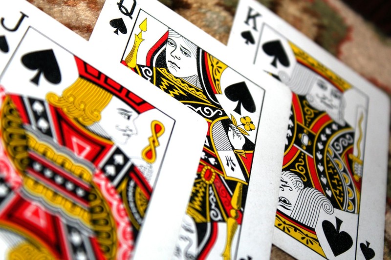 Close-up of three overlapping spade suit face cards — Jack, Queen, and King — on a textured surface