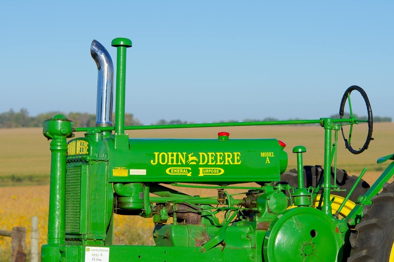 A classic green John Deere Model A tractor in a golden farm field under a blue sky