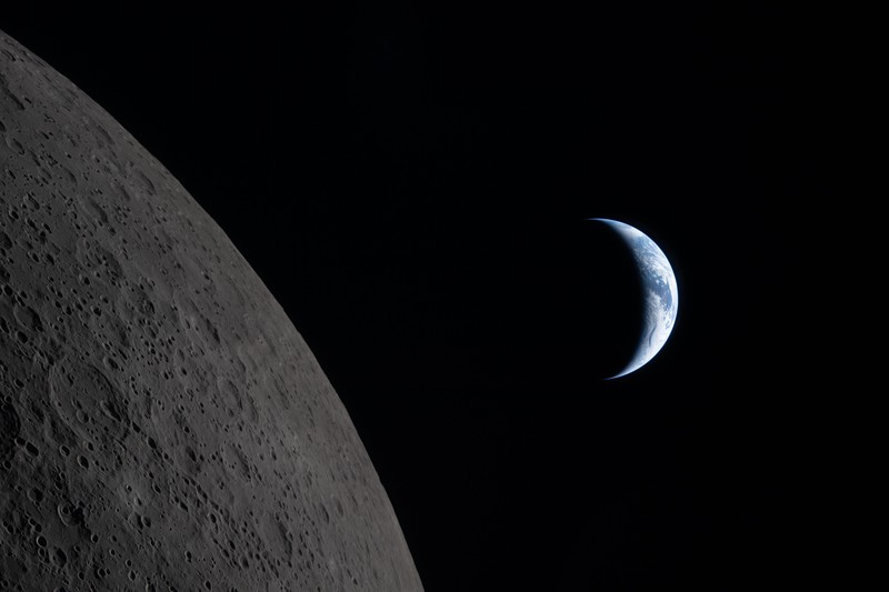 The Moon dominates the foreground as a tiny crescent Earth appears in the distance, photographed by the Artemis II crew during their lunar flyby.
