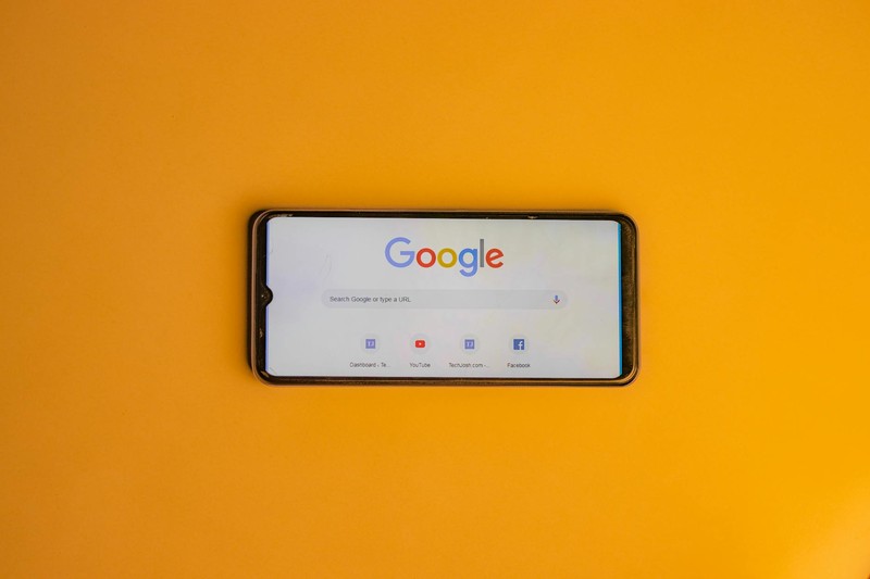 A smartphone displaying the Google search homepage against a vibrant orange background