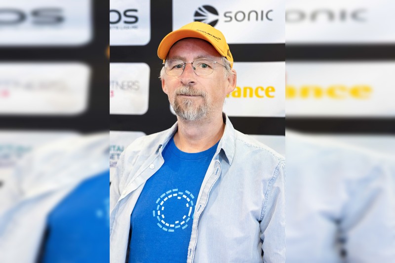 Portrait of cryptographer Adam Back wearing a yellow cap and glasses at a conference event