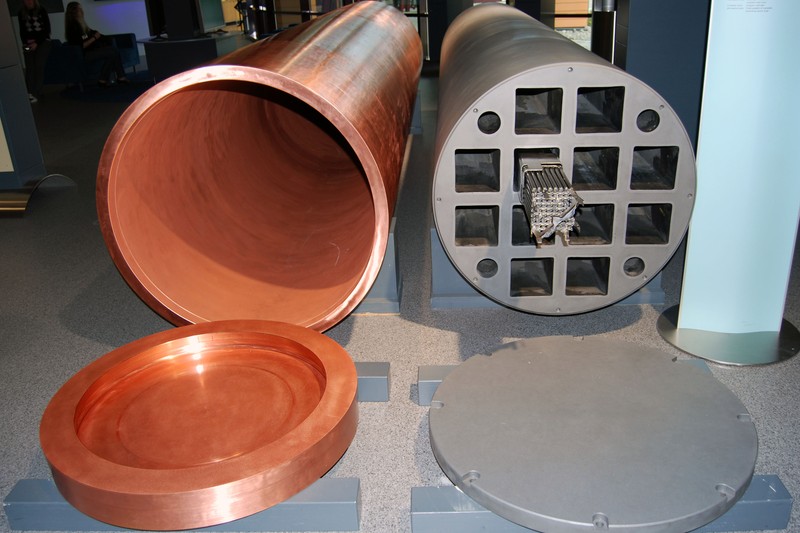 Two copper nuclear waste storage canisters with their lids, displayed in an industrial setting