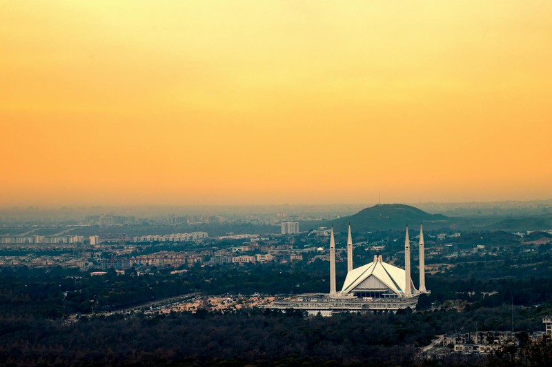 Islamabad's Faisal Mosque silhouetted against a vibrant sunset sky with the cityscape and Margalla Hills in the background