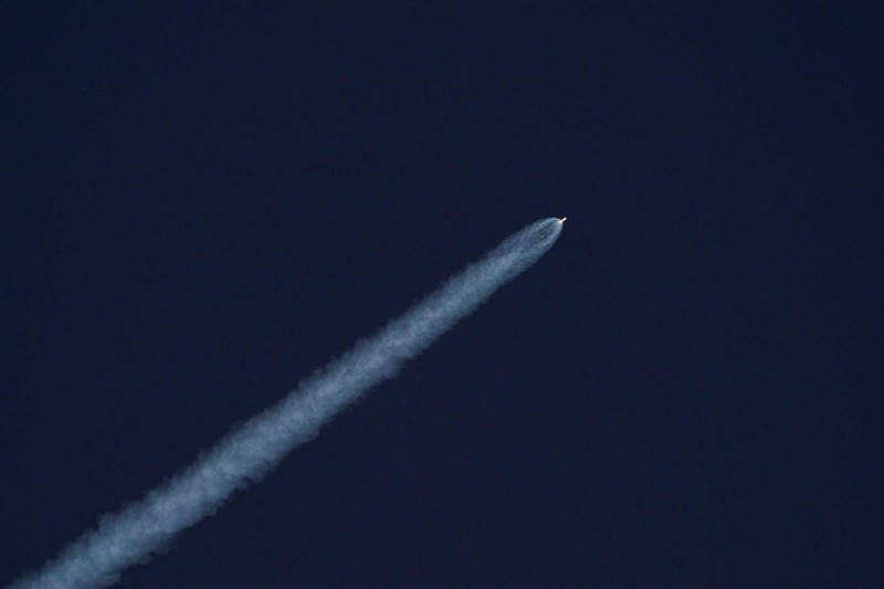 A rocket ascends into a dark sky leaving a thick white exhaust trail