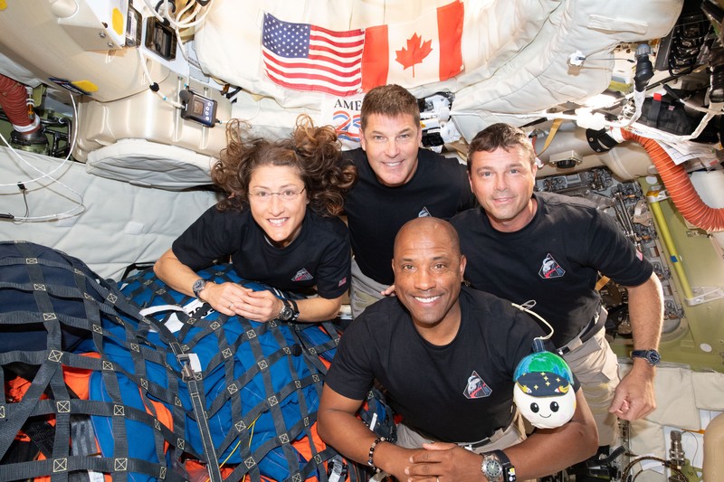 The four-member Artemis II crew poses together inside a spacecraft interior with American and Canadian flags visible above them.