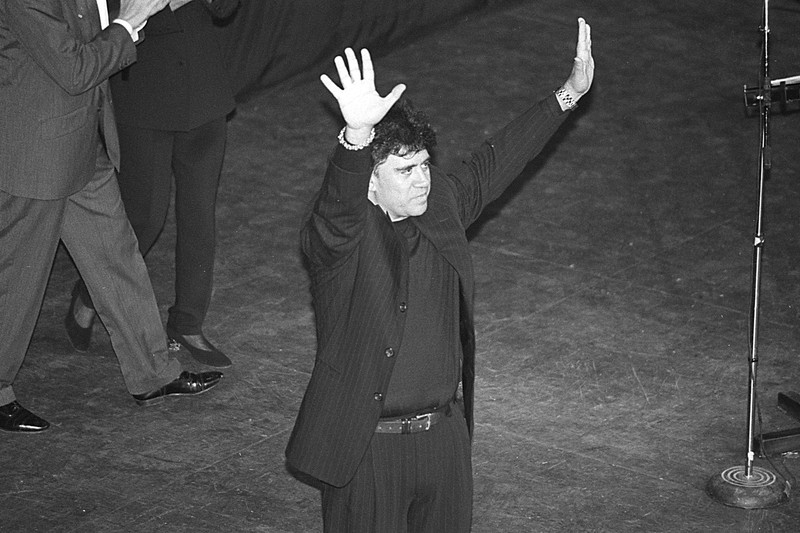 Pedro Almodóvar on stage at a film festival closing ceremony, arms raised in acknowledgment