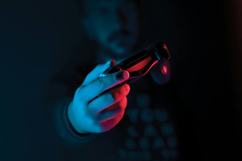 A hand grips a joystick illuminated by dramatic red and blue lighting against a dark background