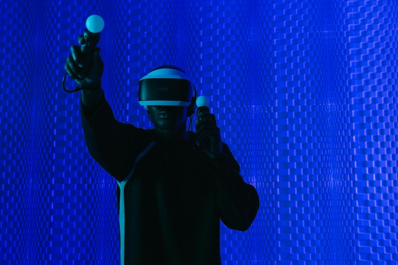 A person wearing a VR headset and holding motion controllers, illuminated by dramatic blue lighting