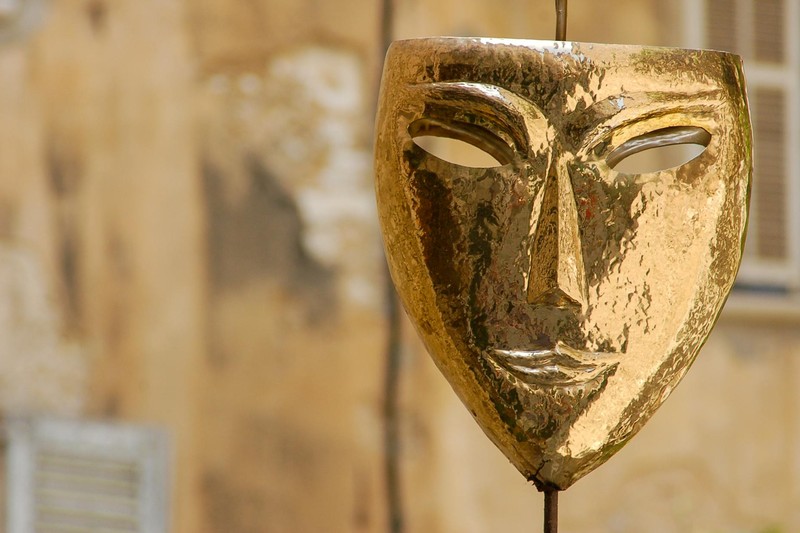 A polished golden theatrical mask suspended against a rustic, weathered wall