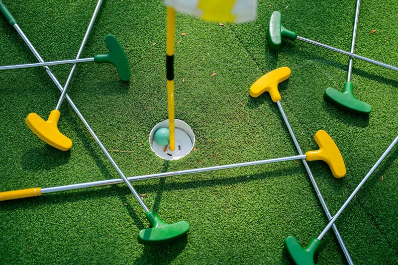 Colorful mini golf putters scattered around a putting hole on bright green artificial turf