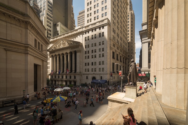 The New York Stock Exchange building on Wall Street with pedestrians and surrounding financial district skyscrapers
