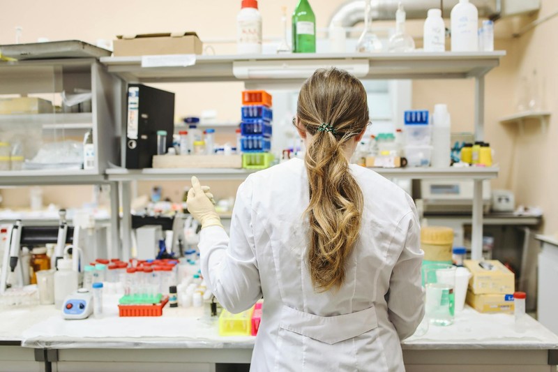 A scientist in a white lab coat working at a laboratory bench surrounded by research equipment and sample containers