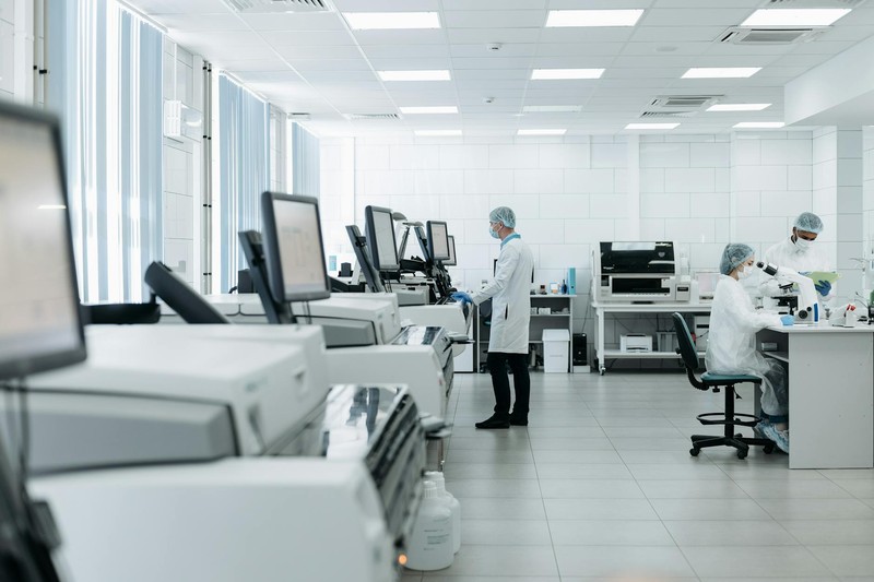 Three scientists in white lab coats conducting research in a modern laboratory with computer monitors and analytical equipment