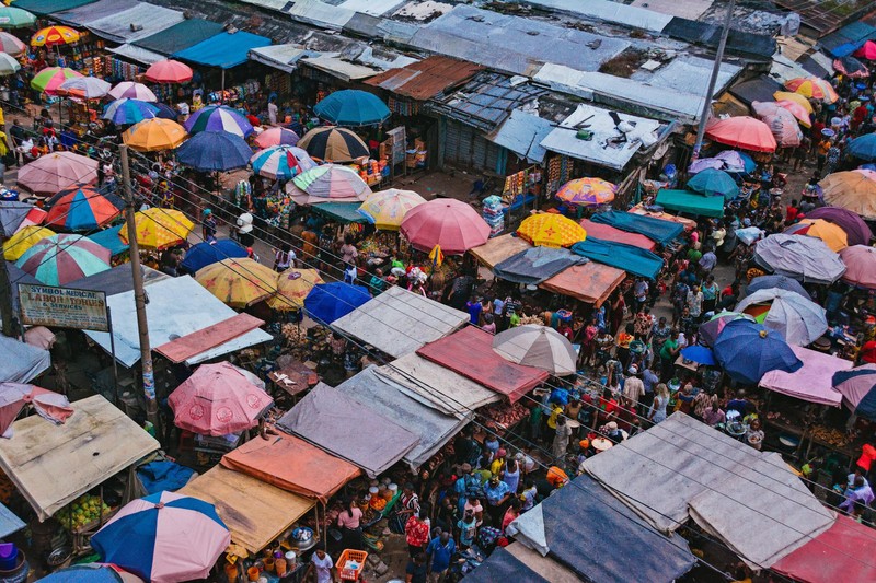 Aerial view of a densely packed open-air market in Nigeria with colorful umbrellas and crowds of shoppers