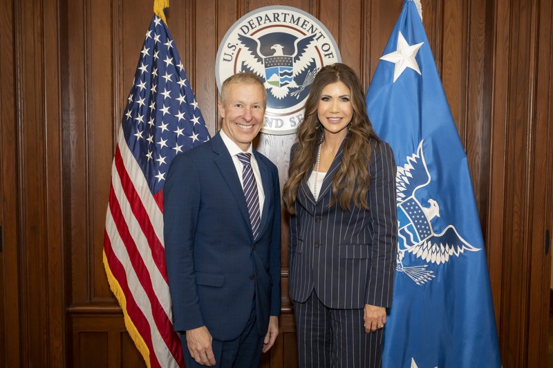 United Airlines CEO Scott Kirby and DHS Secretary Kristi Noem pose for a photo at DHS headquarters with U.S. and departmental flags behind them.