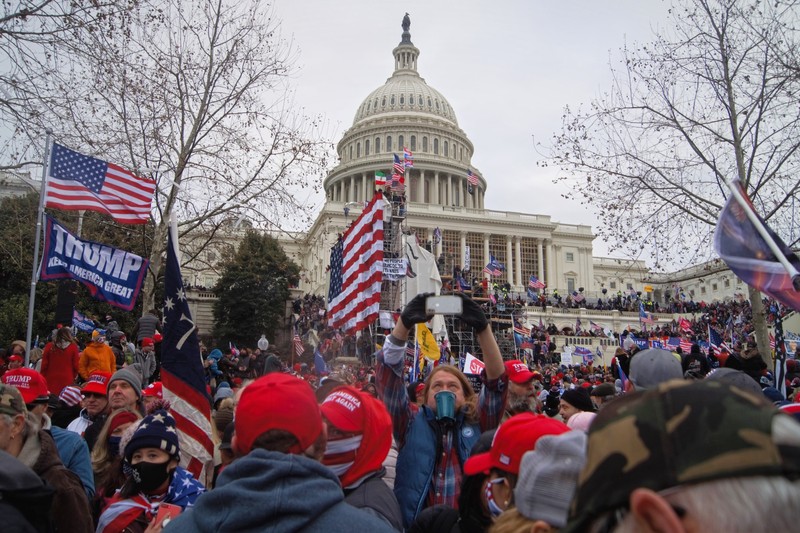 A large crowd of protesters gathers outside the U.S. Capitol building on January 6, 2021, holding flags and signs under an overcast sky.